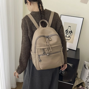 Detail of khaki pebbled leather backpack showing multi-zipper layers and drawstring