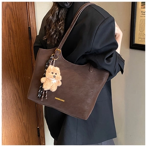 Detail of a dark brown leather tote bag with a plush bear charm and striped ribbon accent