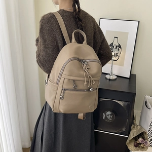 Minimalist beige leather backpack shown on model in a cozy indoor lifestyle setting