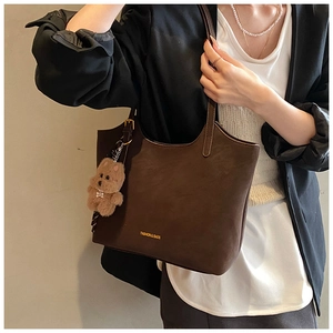 Detail view of dark brown leather tote bag with matte texture and plush bear charm
