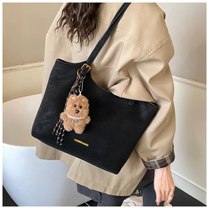 Detail of black matte tote bag with gold hardware and a cute plush bear pendant charm