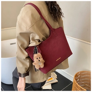 Detail of burgundy leather tote bag with bear charm and gold lettering on shoulder