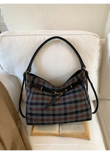 Detail of retro plaid hobo bag with black leather strap and bronze buckle on a white sofa