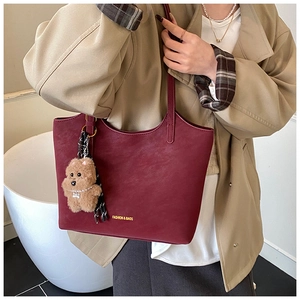 Close-up of burgundy oversized tote bag with plush teddy bear charm and fashion text