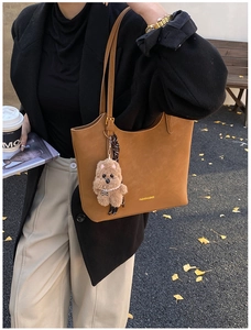 Brown leather tote bag with a plush puppy charm shown in an autumn street setting