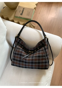 Detail der Woll-Hobo-Tasche mit Karomuster, Ledergriff und goldenen Beschlägen auf Sofa