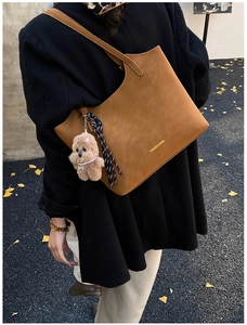 Brown leather tote bag featuring a teddy bear charm and fringe details in a street setting
