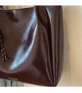 Détail d'un cabas marron foncé avec texture cuir brillant et ornement de cordon tressé