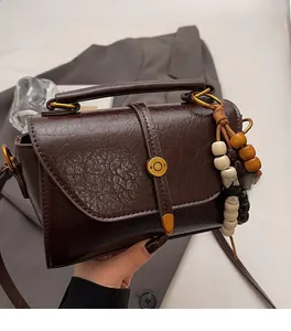 Detail of dark brown vintage handbag with gold clasp and wooden bead charm on a model