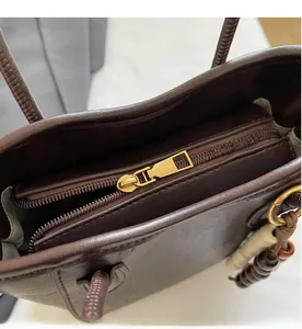 Détail d'un sac à main en cuir marron foncé avec fermeture éclair dorée et breloques de perles