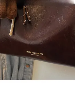 Gros plan du sac cabas en cuir marron brillant avec logo doré et pompon doux
