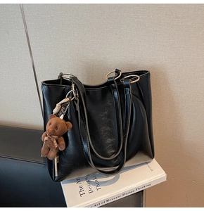 Détail d'un cabas noir en cuir verni avec un pendentif ours et deux bandoulières souples