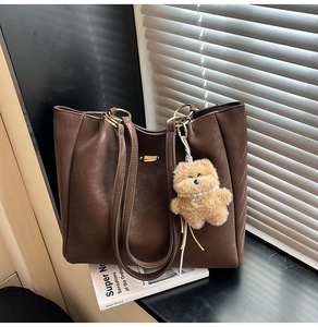 Detail of dark brown tote bag featuring golden hardware and a cute puppy plush charm
