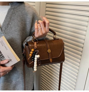Detail of a brown leather Boston bag with vintage beads and glossy PU finish