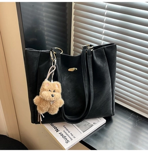 Close-up of black PU leather tote bag with gold metal hardware and brown plush bear charm