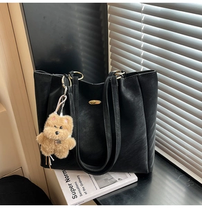 Macro detail of black tote bag with gold logo and a cute brown plush bear charm
