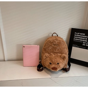 Vue détaillée du sac à dos ours en peluche marron à côté d'une tablette pour la taille