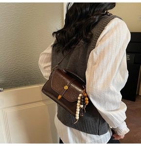 Detail of a dark brown oil-wax leather square crossbody bag with a beaded wood charm