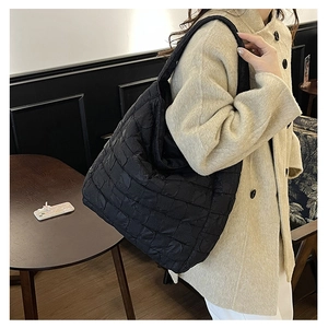Quilted black puffer hobo bag with padded lattice pattern worn as a shoulder bag