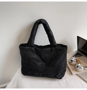 Detail of black pleated fabric tote bag showing textured embroidery material and soft handle