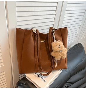 Close-up of brown leather tote bag with a plush bear charm and gold metal buckle detail