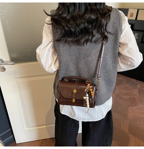 Detail of a dark brown crossbody Boston bag with a beaded tassel on a model
