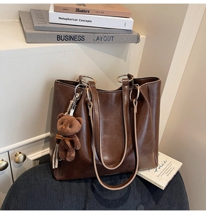 Détail d'un sac cabas marron en cuir huilé avec anneau doré et pendentif ours en peluche