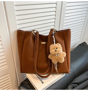 Brown leather tote bag featuring a gold buckle and a cute plush bear charm detail