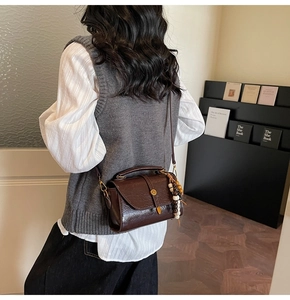 Close-up of a dark brown glossy leather crossbody bag featuring unique beaded charms