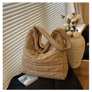 Detail of beige quilted tote bag showing square stitching and wide shoulder strap texture