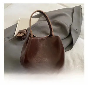 Détail d'un sac seau en cuir marron foncé brillant avec logo et bandoulière texturée