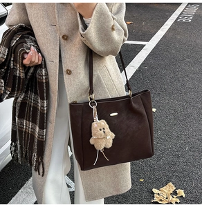 Detail view of large dark brown tote bag with plush bear pendant on an autumn street