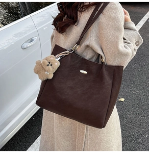 Close-up of a large dark brown tote bag with a cute bear charm on a female model