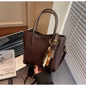 Détail du sac seau en cuir marron foncé avec pompon en bois et ferrures dorées vintage