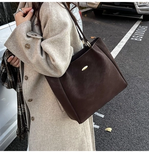 Dark coffee large tote bag in suede texture styled with a beige coat in an outdoor setting