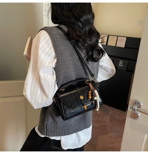 Detail of black glossy wrinkled shoulder bag featuring golden round clasp and beaded charm