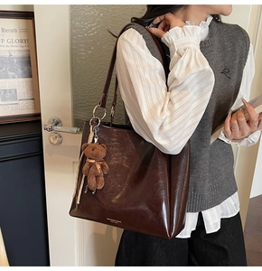 Détail d'un sac cabas marron foncé en cuir brillant avec un charmant ours en peluche