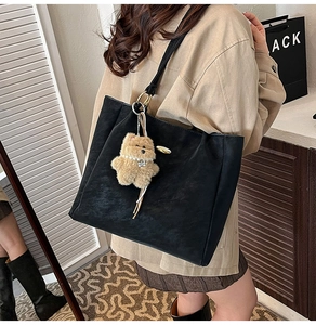 Detail of large black tote bag with matte texture and cute plush bear charm accessory