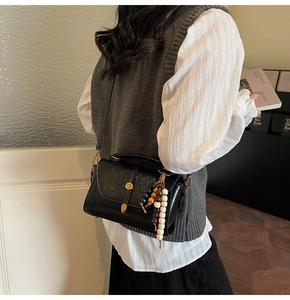 Detail of black embossed PU crossbody bag with metal twist lock and wooden bead pendant