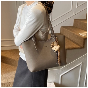 Detail view of a taupe leather tote bag with a leopard print bear charm on a model