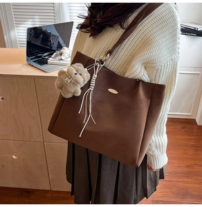 Detail of coffee brown leather tote bag with a cute plush dog charm and white tassel