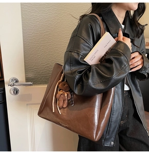 Détail d'un grand sac cabas en cuir marron avec un joli petit ours en peluche sur l'anse