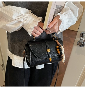 Close-up of black pleated crossbody bag with decorative wooden beads and gold hardware