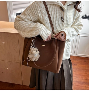 Brown suede tote bag detail featuring slender shoulder straps and a plush bear pendant