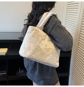 Detail of embroidered floral patterns on beige silk tote bag with golden cloud motifs
