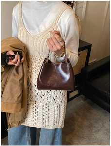 Détail d'un sac seau marron foncé brillant avec texture en cuir poli et anse à main élégante