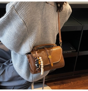 Brown vintage shoulder bag with beaded pendant and retro gold hardware on grey knitwear