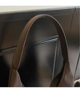 Detail of a dark brown frosted suede shoulder bag with a wide seamless strap design