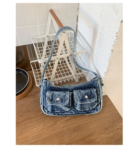 Detail of light blue washed denim shoulder bag with silver snap pockets on wooden table