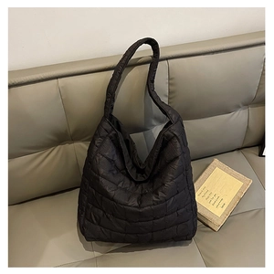 Detail of black quilted puffer tote bag on grey sofa showing texture and glossy finish